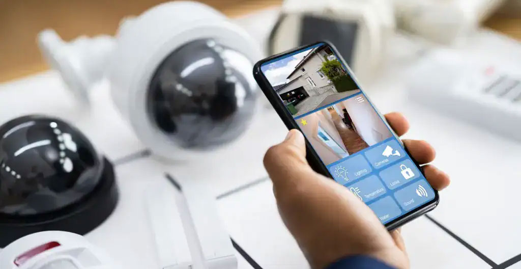 Famille française vérifiant l'application de sécurité connectée sur smartphone avant départ en vacances avec enfants et bagages